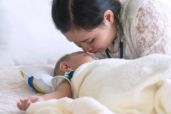 息子がベッドで寝ている間 幸せな若い母親は彼女のかわいい赤ちゃんの顔に愛をキスします 母の日のコンセプト — ストック写真