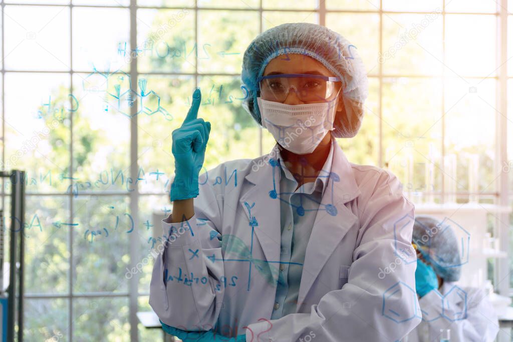 Laboratory science concept. Scientific young woman wear blue gloves and lab coat standing front board glass while learn research in the lab.Scientist with protective eyeglasses holding her finger up. 