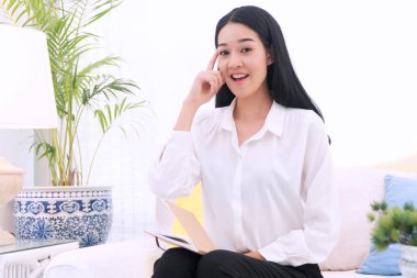 Beyaz koltukta oturan mutlu genç kadın yeni bir fikir düşünürken parmağıyla kafasını işaret ediyor. Kitabı olan güzel bir kadın. Fikri düşün. Evdeki oturma odasını yönet.. 