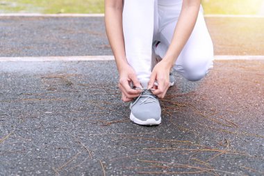 Genç koşucu kadın parkta koşmak için ayakkabı bağcığı bağlıyor ve ellerine odaklanıyor. sağlıklı yaşam tarzı ve spor kavramları.