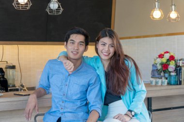 Kafede kahve içen genç ve mutlu bir çift. Neşeli genç bir kadın erkek arkadaşını işaret ediyor açık kahve dükkanında bir şey görüyor.. 