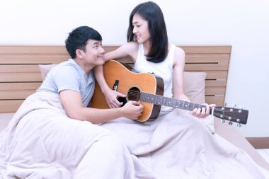Çiftler yatakta birlikte gitar çaldılar. Romantik koca karısına gitar çalmayı öğretirken ikisi de evde birlikte oturuyor. İlişki çifti kavramı.
