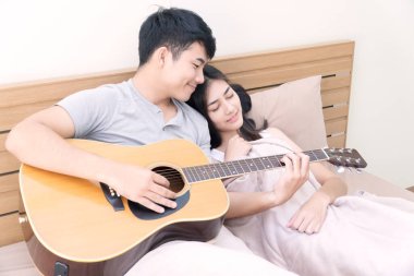 Aşık romantik genç bir çift yatak odasında kız arkadaşına gitar çalıyor. Yakışıklı adam evde karısı için akustik gitarla müzik çalıyor. İlişki kavramı.