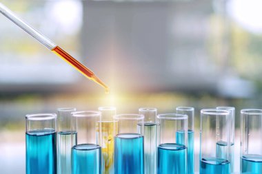 Bilimin test tüpü. Laboratuvar pipeti, deney tüplerinin üzerine turuncu sıvı damlatarak bilimsel araştırma laboratuarında yapılan bir deney için mavi kimyasal çözeltiyle doldurulmuş..