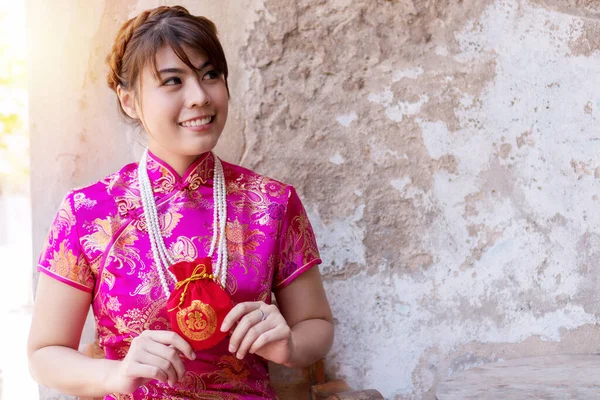 Happy Chinese new year concept. Cheerful smile young woman wear cheongsam dress holding red angpao containing money for luck and prosperity family give for her. Red bag in Chinese means, good luck