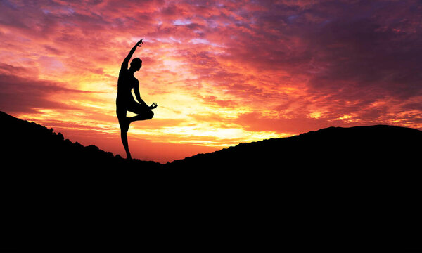 Silhouette of healthy young woman practicing yoga meditation during on background mountain with sky and sunset.