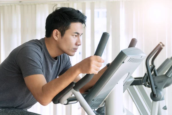 Athlete men, sport exercise concept. Young handsome man training on bicycle machine at gym in morning. People workout on machine in fitness center.