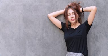 Büyüleyici genç bayan, gri duvar arkasında kalın saçlarını tutarak rahatlıyor. Uzun kahverengi dalgalı saçlarını at kuyruğuyla bağlayan neşeli kız fotokopi alanı olan bir şeye bakıyor..