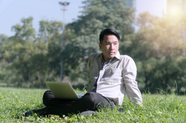 Laptoplu bir iş adamı yeşil çimlerde oturuyor ve parkta bir şeye bakıyor. Yaşam tarzı rahatlama kavramı.