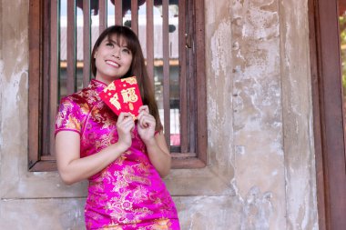 Çekici, mutlu, genç bir kadın, içinde şans ve refah için para bulunan kırmızı ve altın zarflar bulunan Cheongsam koyu pembe elbiseler giyer. Çin Yeni Yıl Kutlama Konsepti
