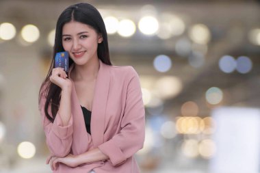 Elinde kredi kartı olan gülümseyen genç bir kadın Bokeh Light arka planında kameraya bakıyor. Çekici bir iş kadını ödeme özgürlüğüyle tatmin olur ve mutlu olur..