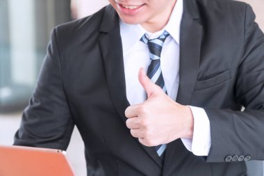 İşadamı iyi bir iş için çalışırken parmağını kaldırdı. Takım elbiseli genç adam başparmağını göstererek iş başarısını temsil ediyor, tamam, harika, tüm iyi şeyleri ve benzerlerini. İş başarılı konsept.