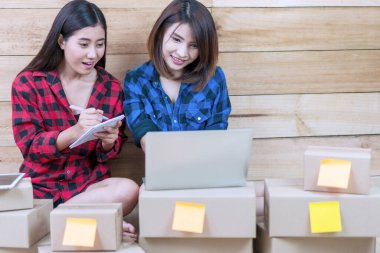 İki genç kadın KOBİ işine başladı. İş kadını takım çalışması. Ev işlerinde çalışmak. Dizüstü bilgisayarla kitap yazma emri. Müşteriye çevrimiçi alışveriş servisi reklamları.