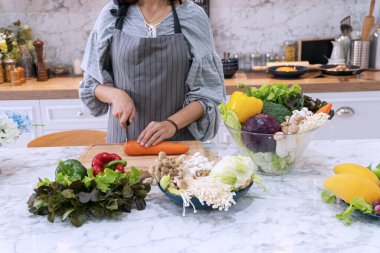 Mutfakta mutfak bıçağıyla havuç kesen çekici bir kadın. Şef sebzeleri yemek olarak keser..
