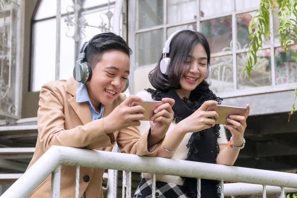 Kulaklıklı mutlu ergen oğlan ve genç kız akıllı telefondan müzik dinliyor ve dışarıda video oyunları oynuyor. Teknoloji konsepti
