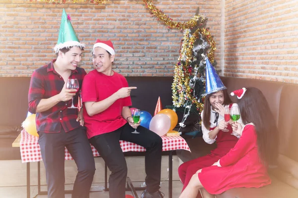 Group of cheerful asian young people friends party celebrating Christmas or Happy new year. Cheerful handsome man and young woman holding glass of green and red drinking wine or champagne.