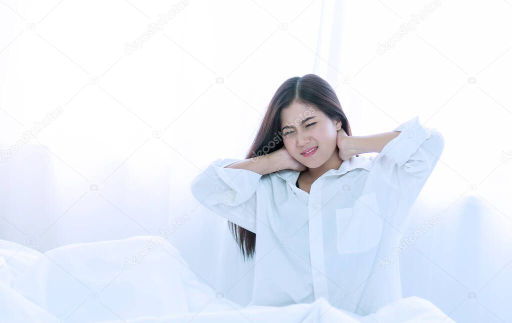 Healthy physical concept. Attractive young woman wake up in the morning on white bed with spine shoulder painful. She hands caught with her neck suffering. Have copy space.
