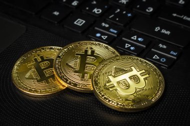 Masadaki siyah dizüstü bilgisayarda üç Bitcoin madeni para