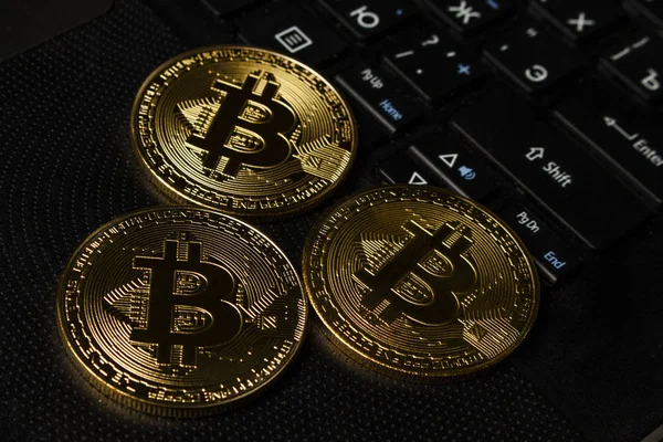 Masadaki siyah dizüstü bilgisayarda üç Bitcoin madeni para