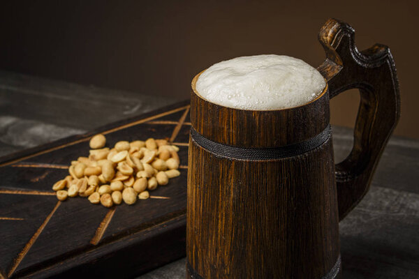 Beer in a wooden mug with peanuts on the board