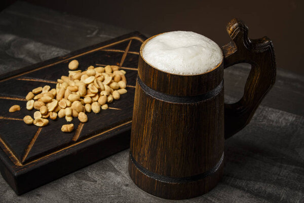 Beer in a wooden mug with peanuts on the board