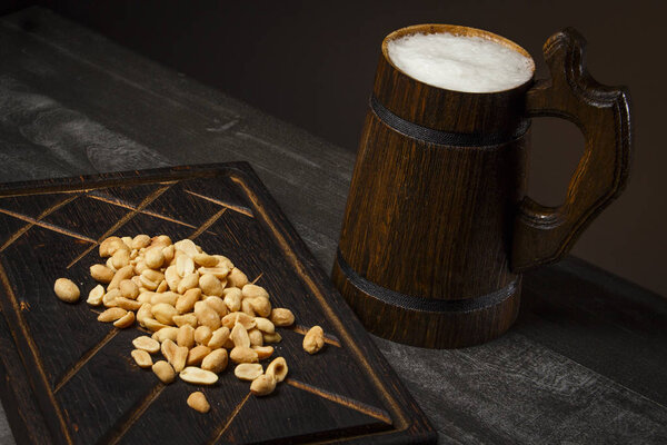Beer in a wooden mug with peanuts on the board