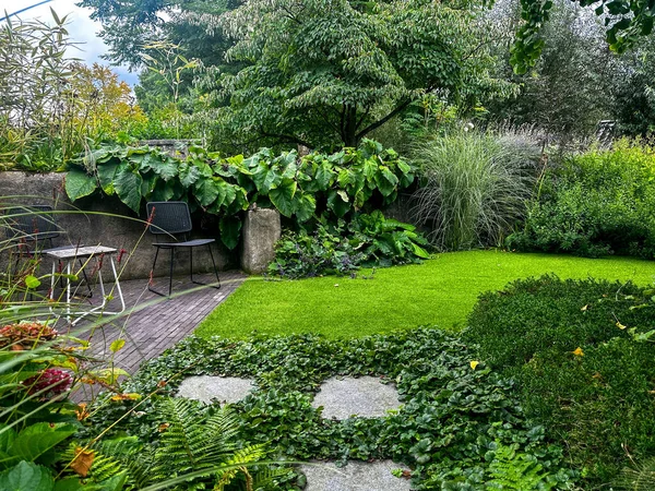 Shaded garden corner. Ferns, ornamental grasses, and shrubs create a peaceful space. Chairs and stone path add charm to the natural design