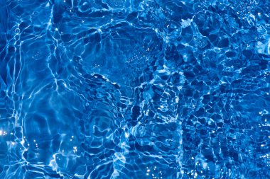 Yüzeyinde dalgalanmalar olan mavi su. Defocus bulanık mavi şeffaf, berrak, durgun su yüzeyi dokusu sıçrama ve kabarcıklarla bulanıklaştırılmış. Parlak desenli arka planda su dalgaları.