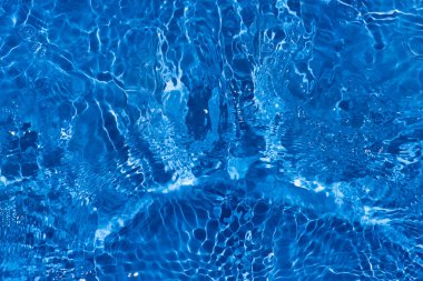 Yüzeyinde dalgalanmalar olan mavi su. Defocus bulanık mavi şeffaf, berrak, durgun su yüzeyi dokusu sıçrama ve kabarcıklarla bulanıklaştırılmış. Parlak desenli arka planda su dalgaları.