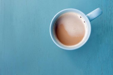 Pastel mavi ahşap zemin üzerinde mavi bir fincan kahve süt