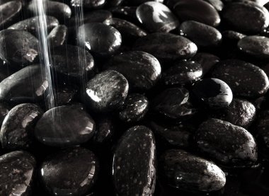 Yuvarlak siyah taşın parlak yüzeyi şelalenin yanında.