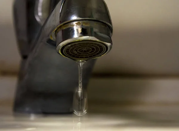 Leaking water drops from old rust and stained faucet