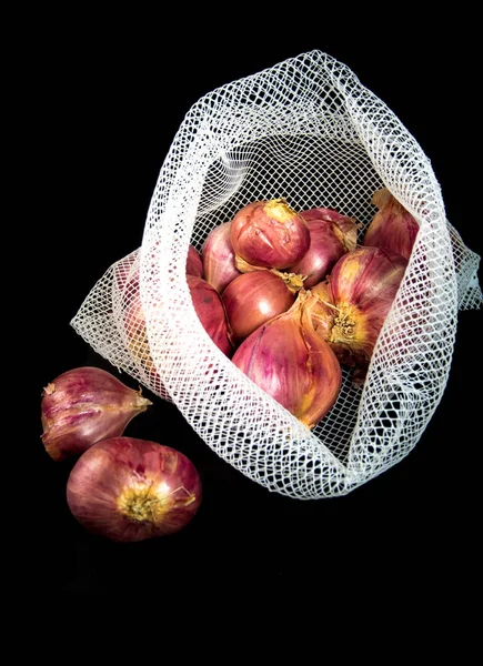 Rote Zwiebeln in Netztasche und einige auf dem Boden isoliert auf schwarzem Hintergrund — Stockfoto