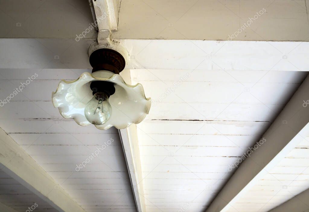 an incandescent lamp in the ancient glass lamp hang on the wooden beam under the second floor of an old wooden building