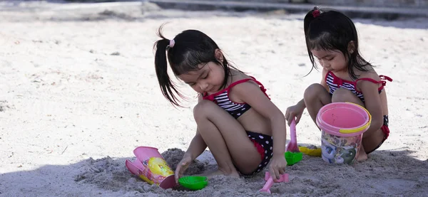 Lindo asiático hembra niño gemelos mientras jugando en arena en un playa — Foto de Stock