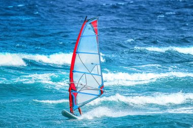 su sporları: rüzgarlı bir yaz günü dalga sürme kırmızı ve mavi yelken ile bir sörfçü.