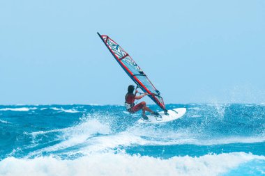 Su sporları: güneşli bir yaz öğleden sonrasında dalgalarda sörf yapan rüzgar sörfçüsü.