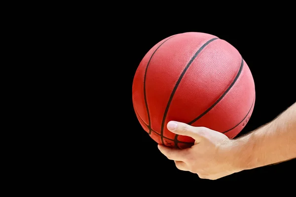 a man holds in his hand a basketball game ball on a dark background