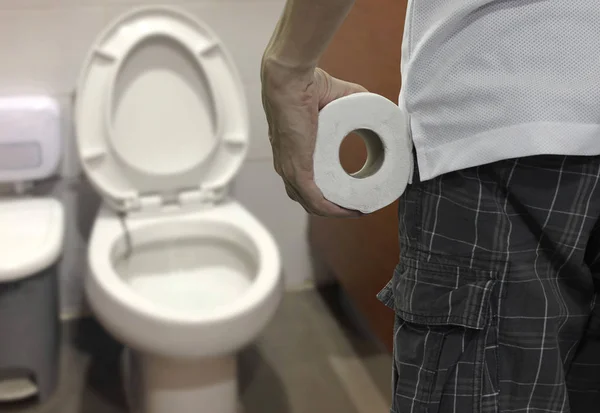 Mão segurando papel higiênico rolo e entrar no banheiro . — Fotografia de Stock