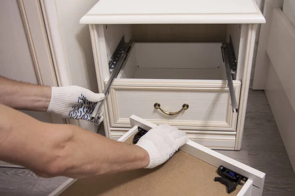 Repair and installation of furniture in the room. Male workers hands in white gloves