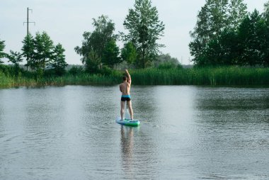 Bir adam birer kürek ve yüzer bir orman göl üzerinden bir Sap tahta üzerinde duruyor,