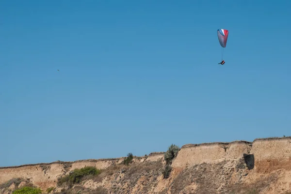 Paraglider hovering over the cliff and the landscape of the sea, soaring on the rising air, extreme and entertainment,