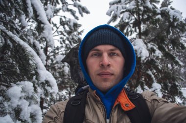 mavi kapüşonlu bir erkekte bir selfie kış orman arka plan ağaçlar, karla kaplı bir yürüyüş ve kış orman, doğa ile birlik üzerine alır,