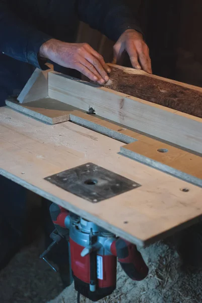 Τα χέρια του ένα παλιό ξυλουργός, εργασίας ολόσωμες φόρμες ισοδυναμεί ένα ξύλινο μπαρ με ένα άλεσμα μηχάνημα στο εργαστήριο, οι μικρές επιχειρήσεις παραγωγής, — Φωτογραφία Αρχείου
