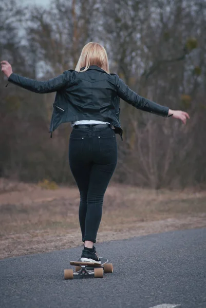 Meisje model skateboarden op een landelijke weg, moderne meisje in lederen jas op een skateboard — Stockfoto