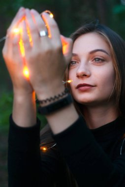 elindeki ışık. Kadınların elleri çelenk tutuyor. Kız elindeki çelenklere bakıyor.,