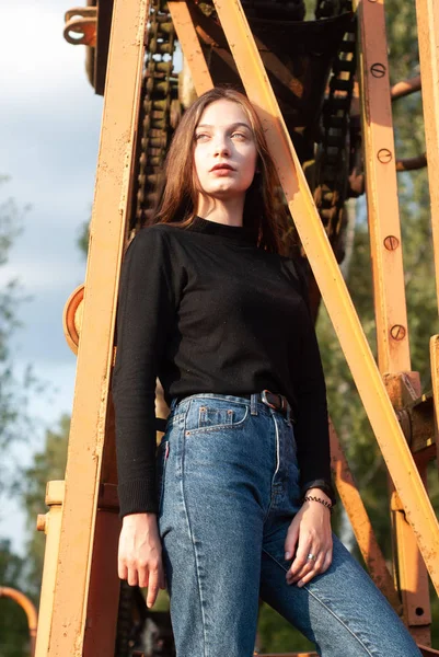 Mladá dívka v modrých džínách na pozadí kovových konstrukcí, — Stock fotografie