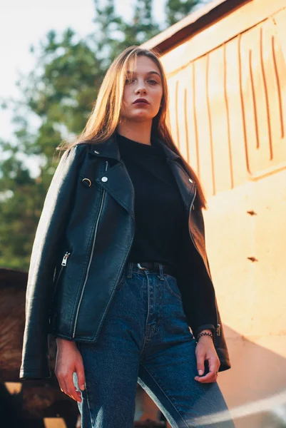 Model v černé kožené bundě s modrými džínami, které se nacházejí venku. moderní chladná dívka — Stock fotografie