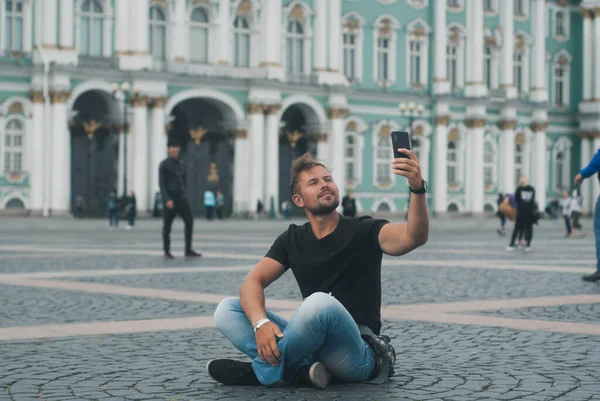 Selfie gülümseyen genç adam St. Petersburg, Rusya 'da. Hermitage 'ın arka planında güzel bir adamın portresi. Kasabada mutlu bir turist