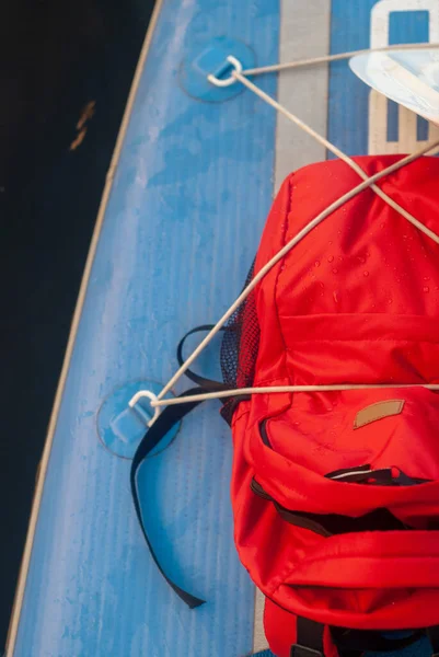 水溜りボード上の赤いバックパック、スポーツ旅行のバックパックを閉じる — ストック写真